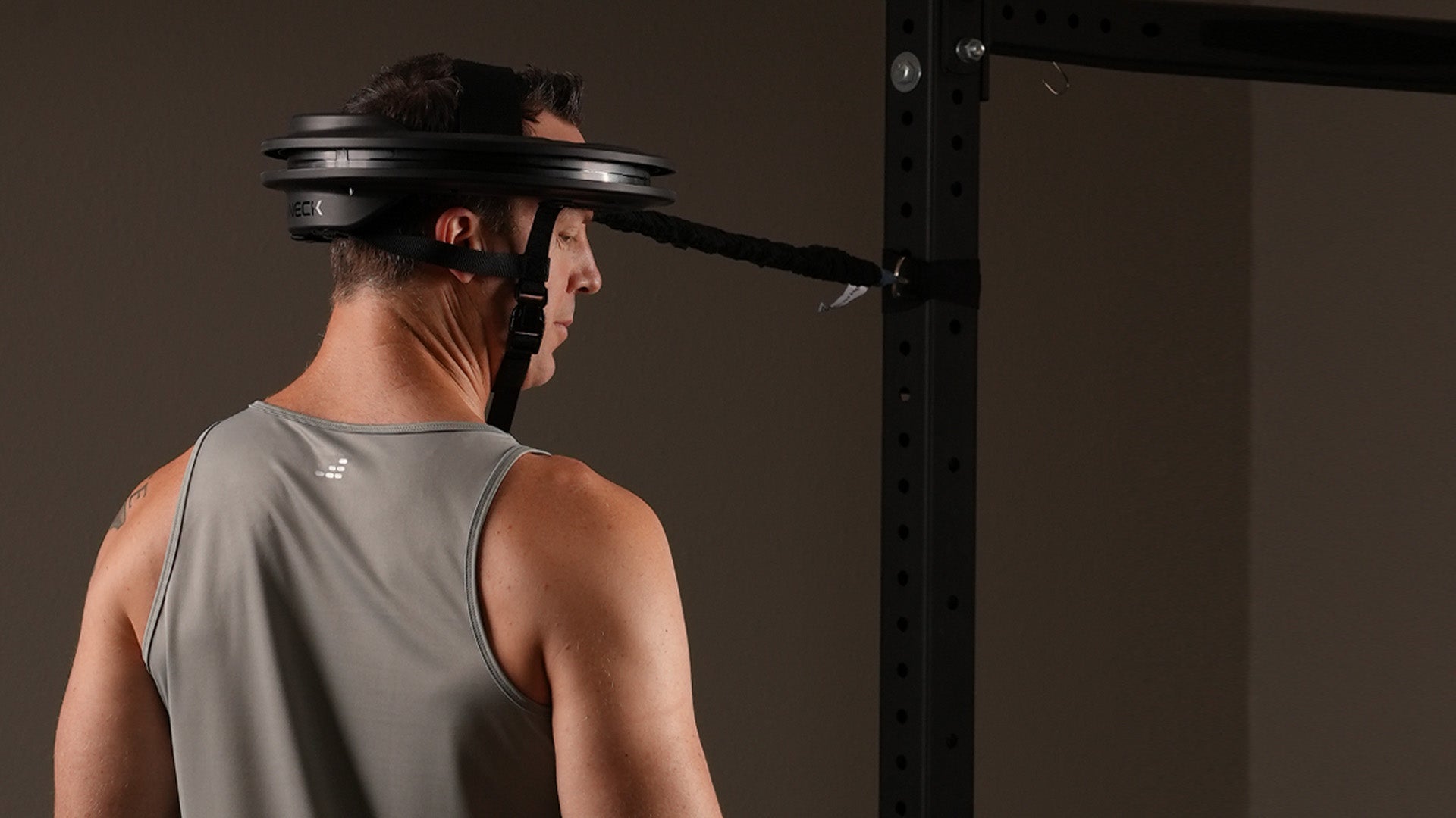 Male wearing tank top and using the Iron Neck 3.0 upon his head.